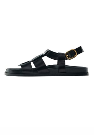 Black flat sandal with wide straps and a gold buckle on the ankle strap, shown in side view on a white background.