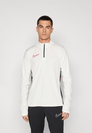 Maglia atletica bianca a maniche lunghe con zip a un quarto, dettagli neri sui lati e logo Nike rosso sul petto. Materiale morbido e elasticizzato.