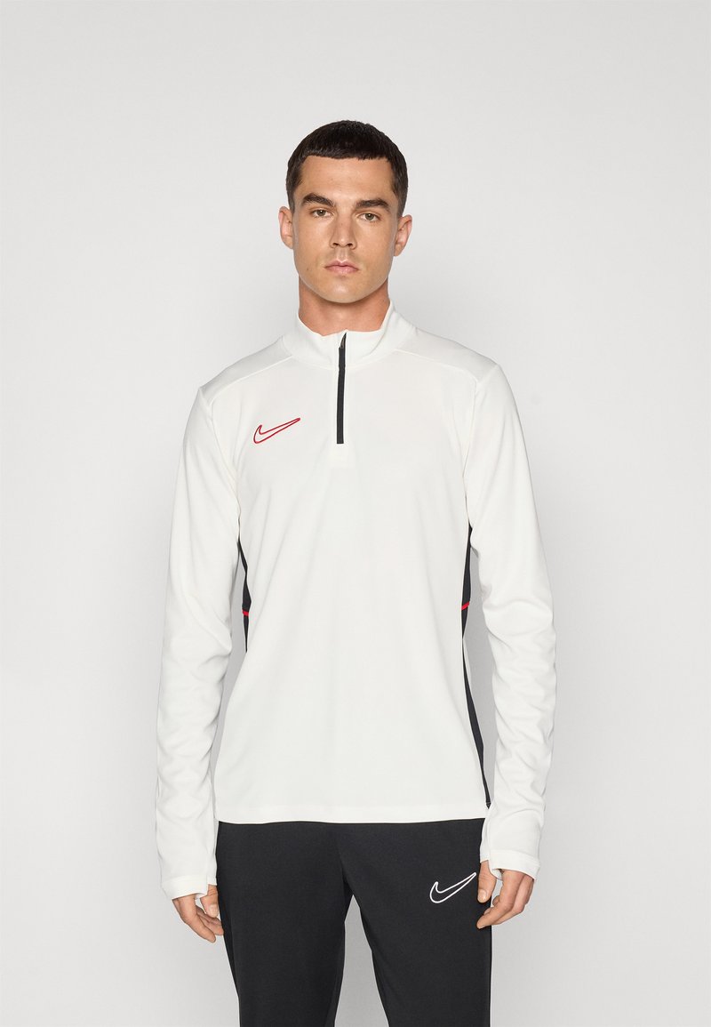 Vit långärmad tränings-topp med kvartslång dragkedja, svarta sidodetaljer och en röd Nike swoosh-logotyp på bröstet. Mjuk, elastisk material.