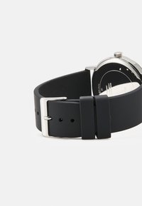 Svart silikonegummirem med sølvmetallspenne. Glatt tekstur, justerbar passform med flere hull, minimalistisk design.