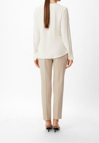 Blouse crème à manches longues avec un col rond, associée à un pantalon beige sur mesure et des talons à brides, vue de dos.