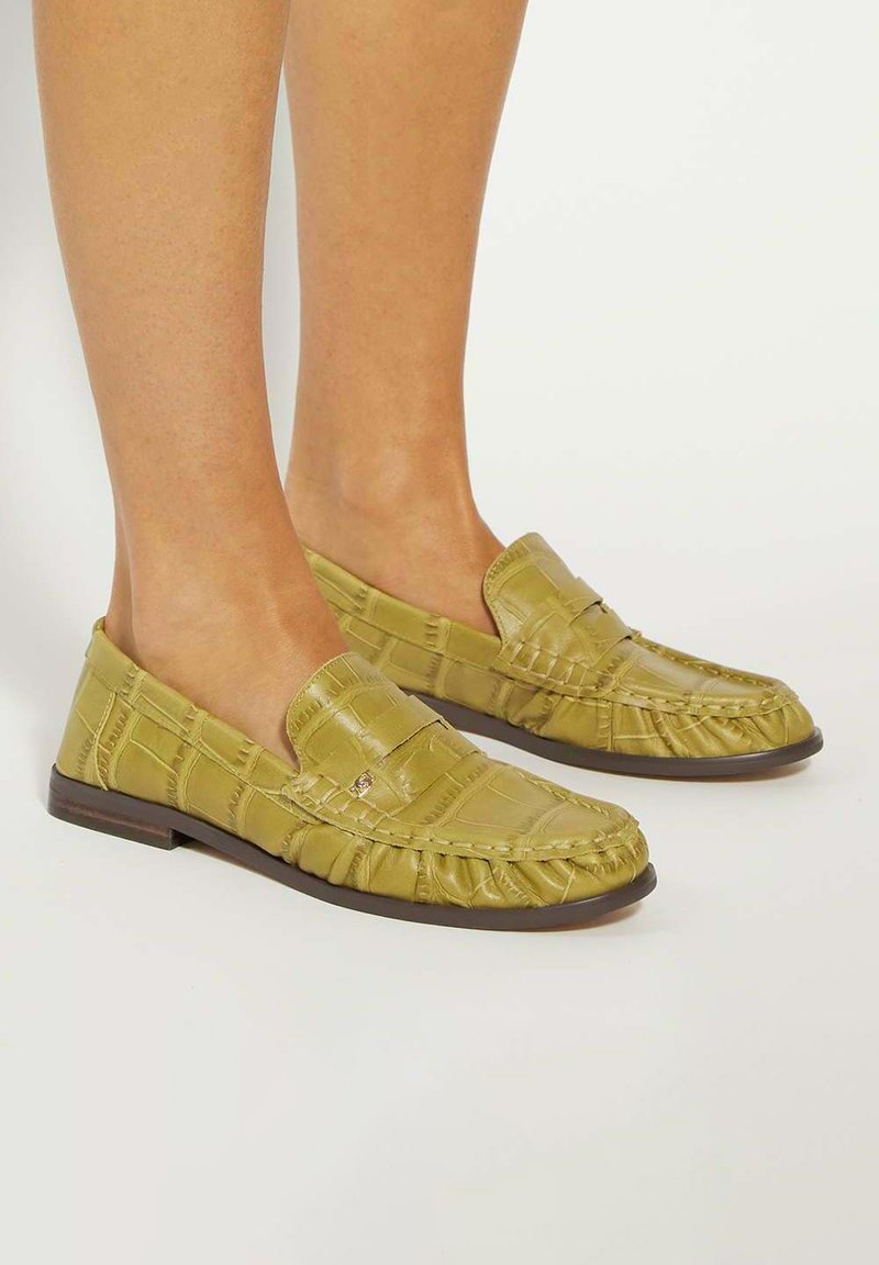 Green faux leather loafers with a textured, croc-like pattern, slip-on design, and a flat brown sole.