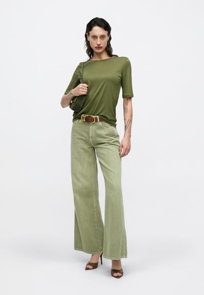 Tricou mulat verde măsliniu, blugi largi verde deschis, curea maro cu accente aurii și sandale maro cu toc înalt. Geantă simplă.