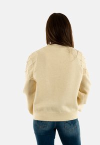 Maglione color crema con una vestibilità oversize e una texture particolare. Presenta dettaglI a forma di diamante sulle maniche, orlo a coste e un tessuto morbido e accogliente.