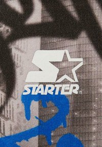 Hvid "STARTER" logo med stjerneaccent på en tekstureret sort og grå baggrund med blå graffiti-lignende detaljer.