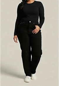 Femme portant un haut noir ajusté à manches longues, un pantalon noir taille haute et des baskets blanches sur un fond clair uni.