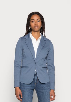 Blue tailored blazer with a smooth texture, single button closure, notch collar, and two front pockets. Worn over a white shirt.