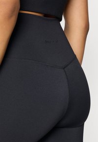 Mustat korkeavyötäröiset legginsit, jotka on valmistettu sileästä, joustavasta kankaasta. Legginseissä on saumaton muotoilu ja hillitty brändäys vyötärönauhassa.