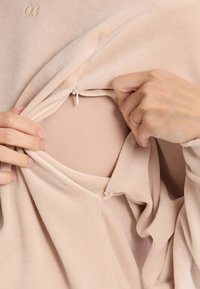 Lichte beige pullover met een zachte, pluche textuur, voorzien van een ritsluiting en een binnenlaag die zichtbaar is door de buitenstof.