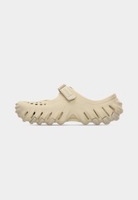 Sabot beige à enfiler avec des trous de ventilation, une bride ajustable au milieu du pied et une semelle texturée robuste pour une meilleure adhérence et un confort accru.