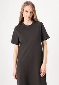 Charcoal grijze t-shirtjurk van zacht katoen. Heeft korte mouwen, een ronde hals en een ontspannen pasvorm met zijopeningen.