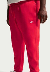 Rode Nike sweatpants met een zachte textuur, voorzien van zijzakken en een wit logo op de linker dij, taps toelopend bij de enkel.