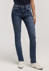 Ciemnoniebieskie, dopasowane jeansy z pięcioma kieszeniami, jasnymi przeszyciami i zapinane na guzik w talii. Połączone z białymi tenisówkami.