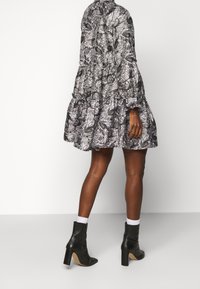 Svart och vit mönstrad klänning med volangnedre och lång ärm, hög hals; kombinerad med svarta ankelskor och vita strumpor.