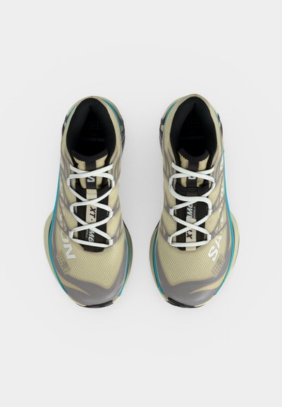 Ζεύγος μπεζ και γκρι αθλητικών παπουτσιών τρεξίματος με άσπρες κορδόνια και τυρκουάζ λεπτομέρειες, φαίνεται από πάνω σε λευκό φόντο.