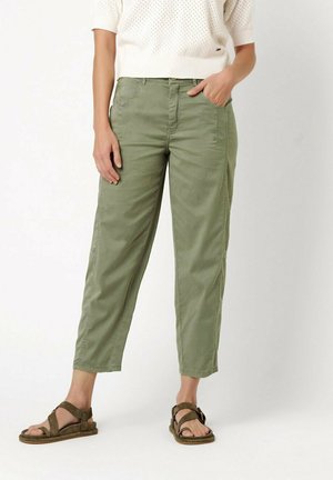 Persona che indossa pantaloni corti verde oliva, top bianco a maniche corte in maglia e sandali verde oliva aperti con cinturini alla caviglia.