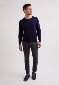 Mörkblå stickad tröja med rund halsringning, bärs med grå slim-fit byxor och blåa sportskor med mörka snören och ljusa sulor.