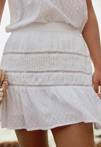 Jupe blanche à volants avec un tissu texturé, présentant des plis horizontaux et des accents en dentelle. Conception légère et décontractée, adaptée aux temps chauds.