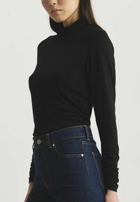 Haut à col roulé noir à manches longues en tissu doux, coupe ajustée, texture lisse, associé à un jean taille haute bleu foncé.