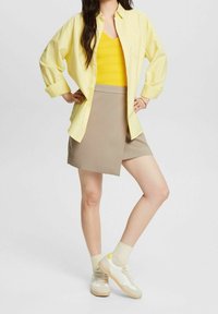 Camicia gialla con bottoni, canotta gialla a trama, gonna avvolgente beige e sneakers bianche con accenti beige. Maniche corte e vestibilità casual.
