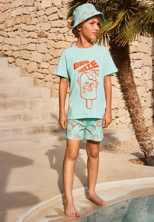 Camiseta de algodón azul claro con gráfico naranja que dice "BRAIN FREEZE"; pantalones cortos aqua a juego con divertidos patrones de helados; sombrero tipo bucket ligero.