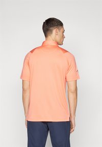 Kortermet polo skjorte i lys korallfarge, med klassisk krage, glatt tekstur og skulderdetaljer for ekstra design. 