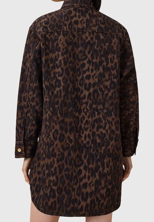 Mujer vistiendo una chaqueta de manga larga con estampado de leopardo y puños abotonados, vista desde atrás sobre un fondo liso.