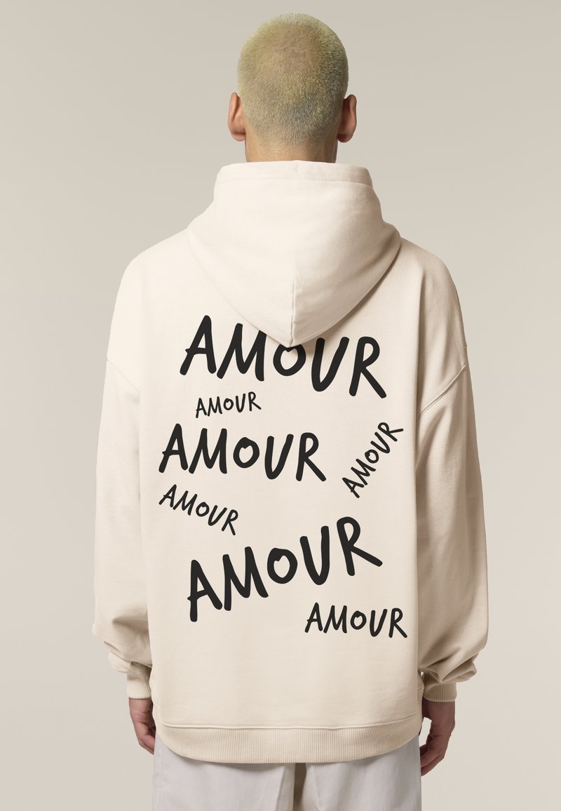 Krémszínű kapucnis pulóver, melyen a hátoldalon különböző méretű, szórt fekete "AMOUR" felirat található. Az anyag lágy és enyhén textúrált.