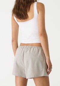 Pantalones cortos de algodón gris con una cinturilla elástica, que presentan un ajuste relajado y bordes rematados, combinados con una camiseta sin mangas blanca.