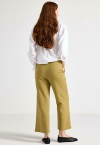 Olivgröna vida byxor med hög midja, tillsammans med en löst sittande vit skjorta. Svarta, öppna sandaler fulländar outfiten.
