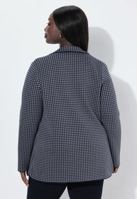 Blazer navy con un piccolo motivo a griglia bianca, design aderente, maniche lunghe e colletto a rever. Tessuto liscio con una sottile texture.