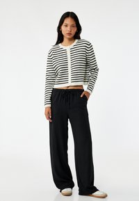 Sort/hvid stribet cropped sweater med rund halsudskæring, parret med løse sorte bukser og hvide sneakers. Glat tekstur og afslappet pasform.