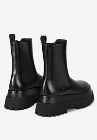 Botas de piel negra hasta el tobillo con paneles laterales elásticos, suela gruesa y suela de goma texturizada para el agarre. Presentan una superficie suave y un diseño minimalista.