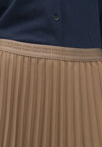 Top bleumarin cu un nasture și fustă plisată bej, având un tiv texturat cu detalii de model geometric.