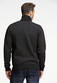 Sort tekstureret pullovertrøje med høj krave, ribbede manchetter og liv, parret med mørke denimjeans.