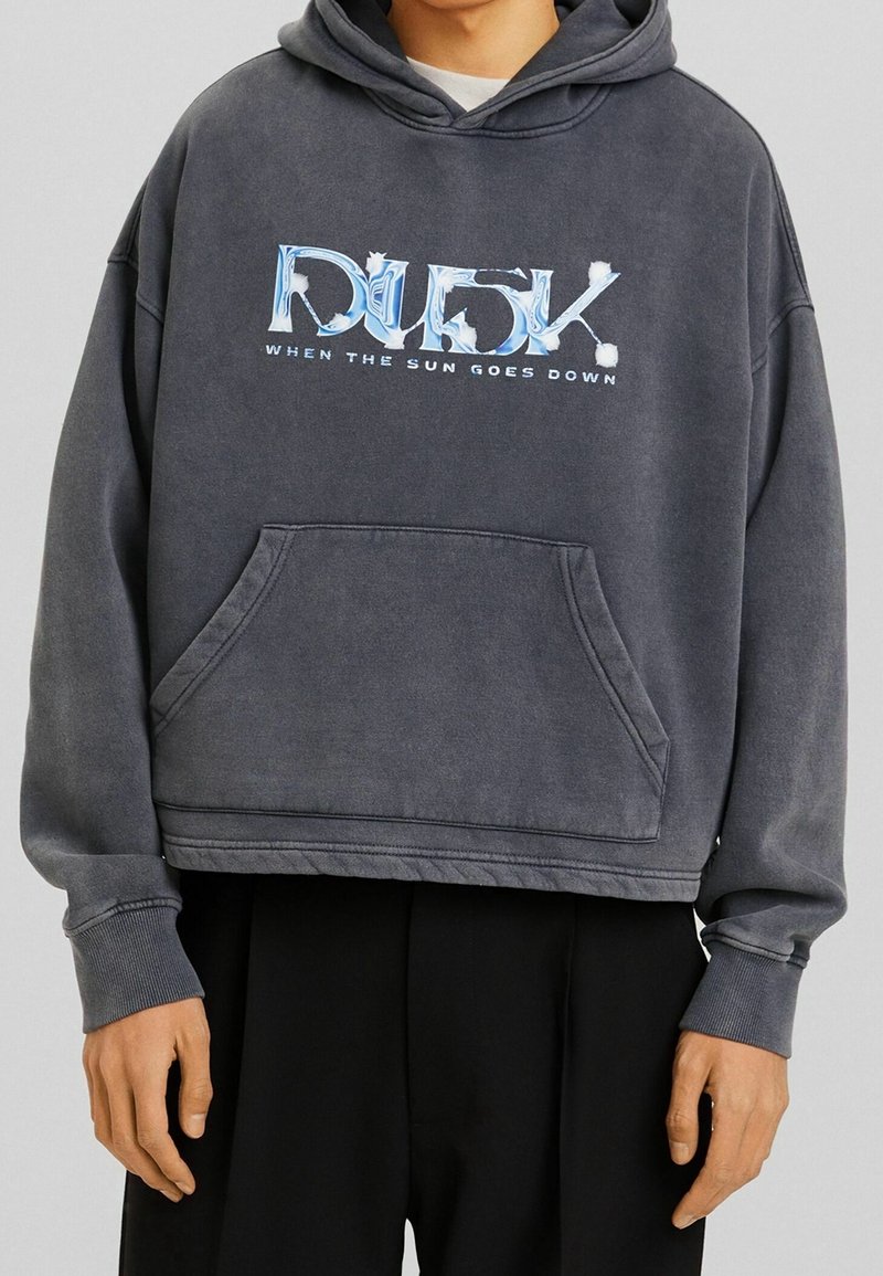 Felpa corta grigio scuro con tasca a marsupio frontale, con stampa grafica di testo blu e bianco che dice "DUSK WHEN THE SUN GOES DOWN."