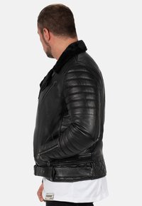 Zwart leren jack met doorgestikte accenten, een schapenvachtkraag, zijritszakken en een getailleerd silhouet, met gestructureerde mouwen.