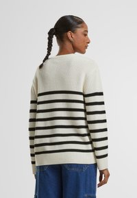 Maglione lavorato a maglia color crema con strisce orizzontali nere, texture a coste e una vestibilità ampia. Presenta un colletto a girocollo e maniche lunghe.