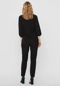 Maglietta nera con maniche a tre quarti, tessuto texturizzato, abbinata a pantaloni neri slim-fit e scarpe con tacco teal, vista da dietro.