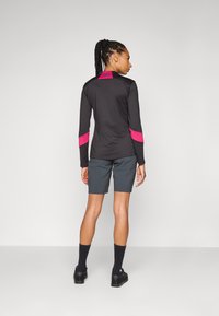 Schwarzes Langarmshirt mit pinken Akzenten, kombiniert mit grauen Shorts. Das Outfit verfügt über feuchtigkeitsableitendes Material und eine lockere Passform.