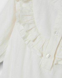 Blusa bianca realizzata in un tessuto texturizzato, con collo arricciato e chiusura a bottoni frontale. Il materiale presenta un delicato motivo per un tocco di maggiore dettaglio.