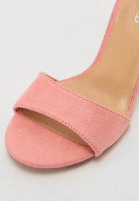 Rožinė suede aukštakulnių šlepečių pora su plačia priekinė juosta, lygiu padu ir matinio paviršiaus apdaila, turinti minimalų siuvinėjimo detalumą.