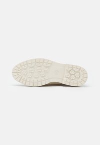 Semelle de chaussure beige avec des crampons profonds présentant des motifs croisés et hexagonaux pour une meilleure adhérence et stabilité.