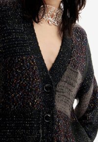 Stickad cardigan med ett flerfärgat mönster i mörka nyanser, djup V-ringning och två stora svarta knappar fram. Strukturerat tyg.