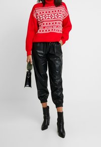 Red knit sweater with a white Fair Isle pattern, paired with black faux leather joggers, and black ankle boots. Green fur handbag accent.