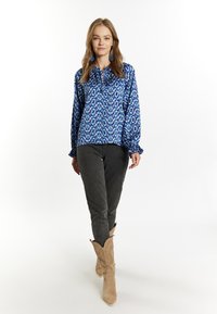 Blusa blu con motivo, dotata di maniche ampie, abbinata a pantaloni grigi scuri e stivali da cowboy color sabbia con cuciture decorative.