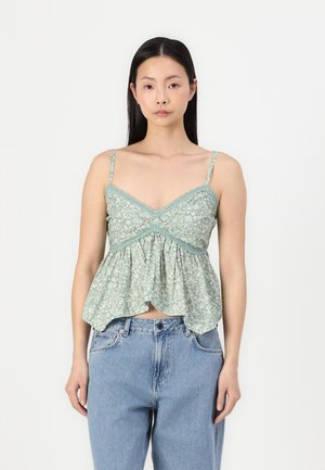 Green floral-patterned camisole with thin straps, gathered waist, and a flared hem. Worn with light blue high-waisted jeans.
