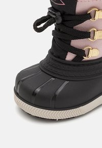 Černá gumová bota s kulatou špičkou, zlatými akcenty a černými tkaničkami. Svršek je vyroben z růžové textilie, s detailním prošíváním a texturovanou podrážkou.