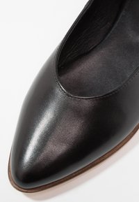 Chaussure plate en cuir noir avec un bout pointu et une coupe basse, présentant une finition lisse et une texture mate subtile. Design minimaliste sans embellissements.