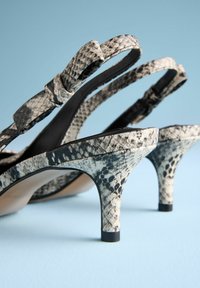 Chaussures à talons hauts noires et blanches à motif serpent, avec des brides fines et un talon courbé, présentant une finition lisse et texturée.